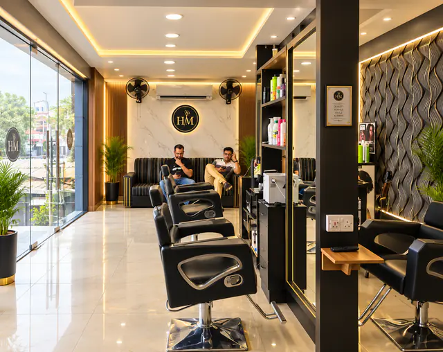 The salon's waiting area: a black striped sofa under the lit HM logo, styling chairs in the foreground and the glass frontage on the left