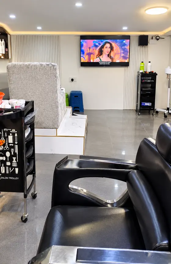 The pedicure station with a raised armchair, a wall-mounted TV and a styling trolley, seen past a black barber chair