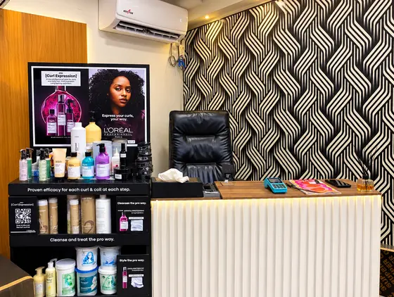 The reception desk in front of the black-and-white woven wallpaper, beside a shelf of L'Oréal Professionnel hair-care products